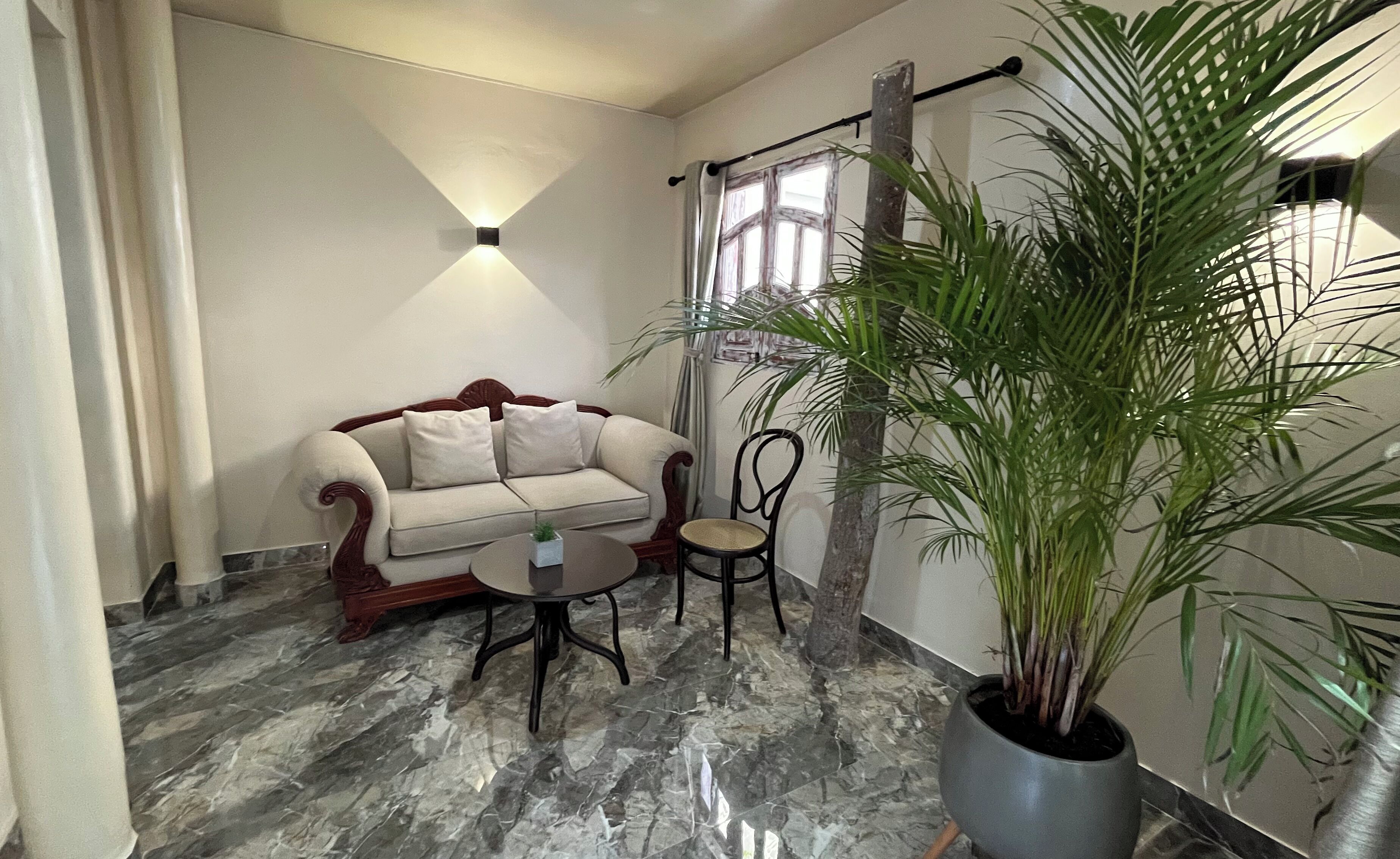 A room with a marble floor, a sofa, a small table, a chair, and a large potted plant.