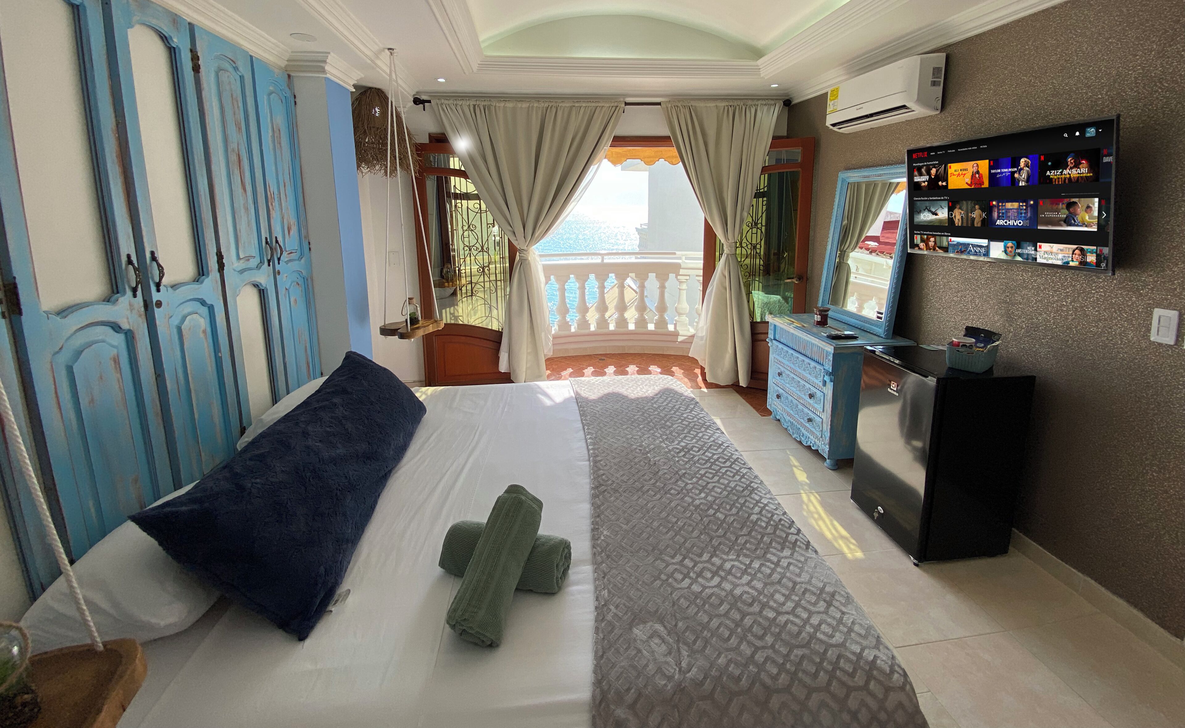 A hotel room with a bed, a dresser, a TV mounted on the wall, and a balcony with a view.
