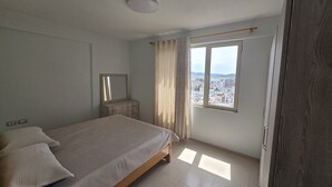 Une chambre à coucher comprenant un lit, une commode, un miroir, une fenêtre donnant sur la ville et une armoire en bois.