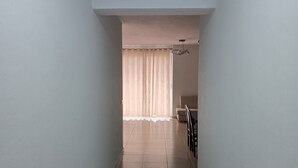 Un couloir étroit avec un sol carrelé, un ventilateur de plafond et une fenêtre avec des rideaux.