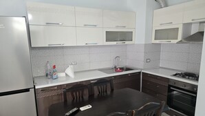 Une cuisine avec des meubles blancs, un réfrigérateur en acier inoxydable, un évier, une cuisinière et une table à manger avec des chaises.
