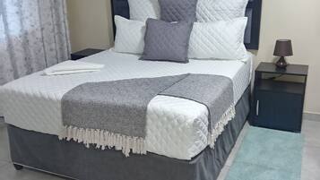 A bed with a headboard, pillows, and a blanket. There is a nightstand with a lamp and a small cabinet.