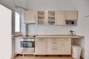 Eine moderne Küche mit Holzschränken, einer Mikrowelle, einem Backofen und einem Mülleimer.