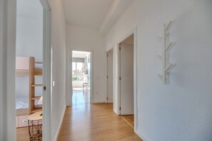 Un couloir avec un plancher en bois, des murs blancs et, au fond, un lit superposé.