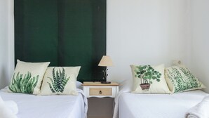 Ein Zimmer mit zwei Betten, jedes mit einem Kissen mit Pflanzenmuster, einem Nachttisch mit Lampe und einer kleinen Schublade.