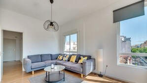 Ein modernes Wohnzimmer mit einem grauen Ecksofa, einem runden Couchtisch und einem großen Fenster mit Blick auf die Stadt.