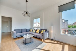 Ein modernes Wohnzimmer mit einem grauen Ecksofa, einem runden Couchtisch und einem großen Fenster mit Blick auf die Stadt.