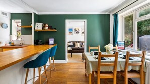 A kitchen with a wooden countertop, blue bar stools, a dining table with wooden chairs, and a view through a window.