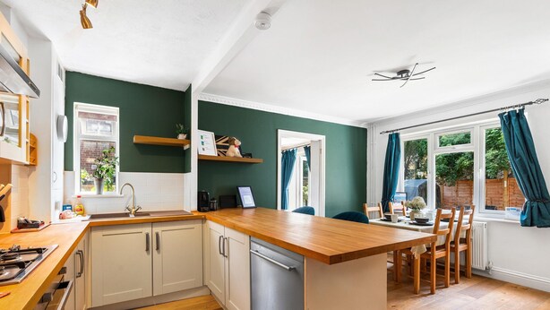 A kitchen with white cabinets, a wooden countertop, a dishwasher, and a dining area with chairs and a table.