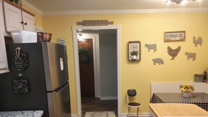 Una cocina con refrigerador, armarios de madera, un lavamanos y una zona de comedor con mesa y silla.