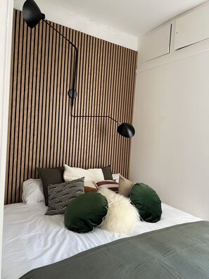 Une chambre à coucher avec un lit, des oreillers, une lampe et un mur recouvert de lattes de bois.
