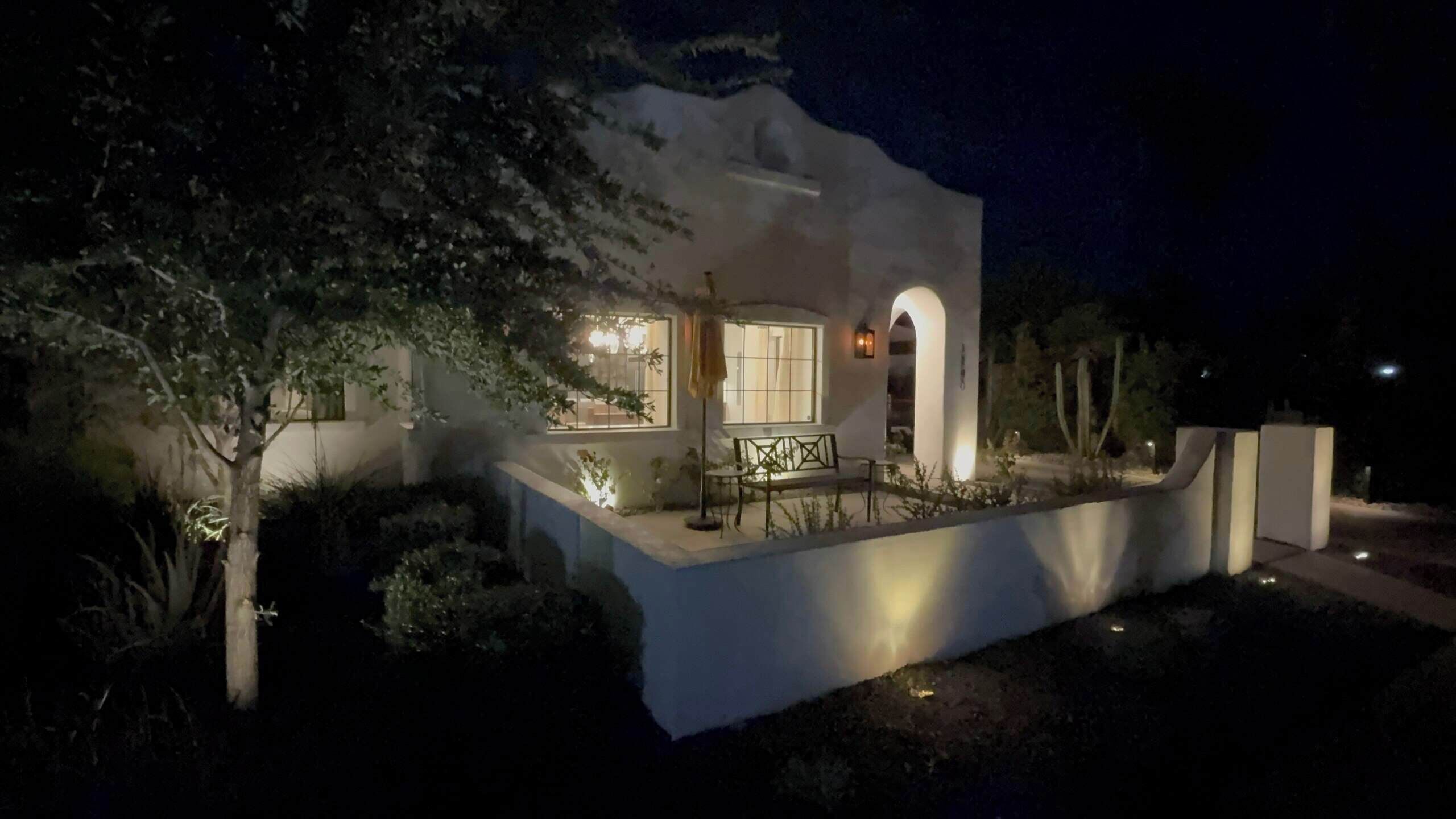 Une maison moderne avec un patio, un banc et un arbre.