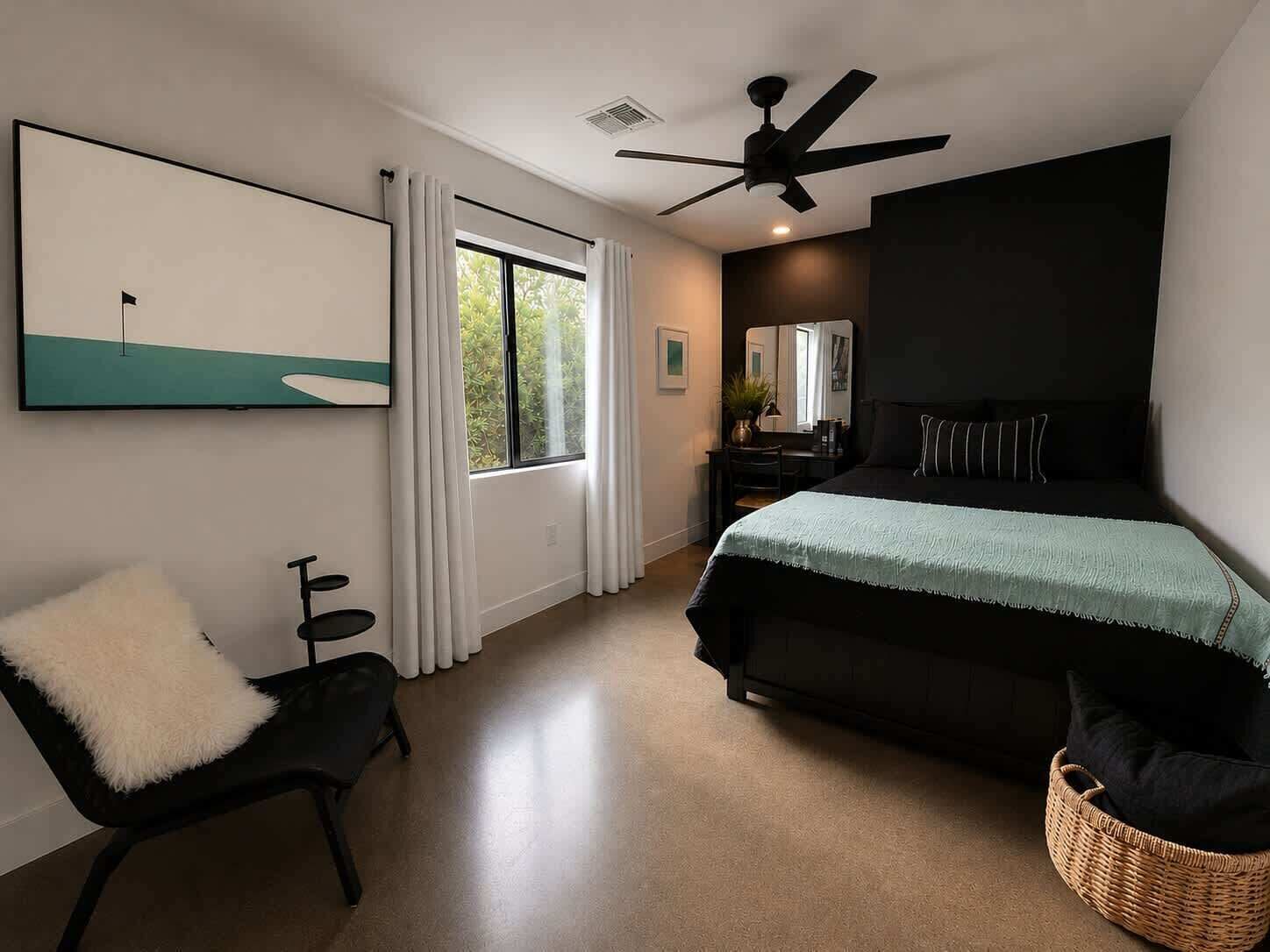 Une chambre à coucher avec un lit, une chaise, un bureau, un ventilateur de plafond et une fenêtre.
