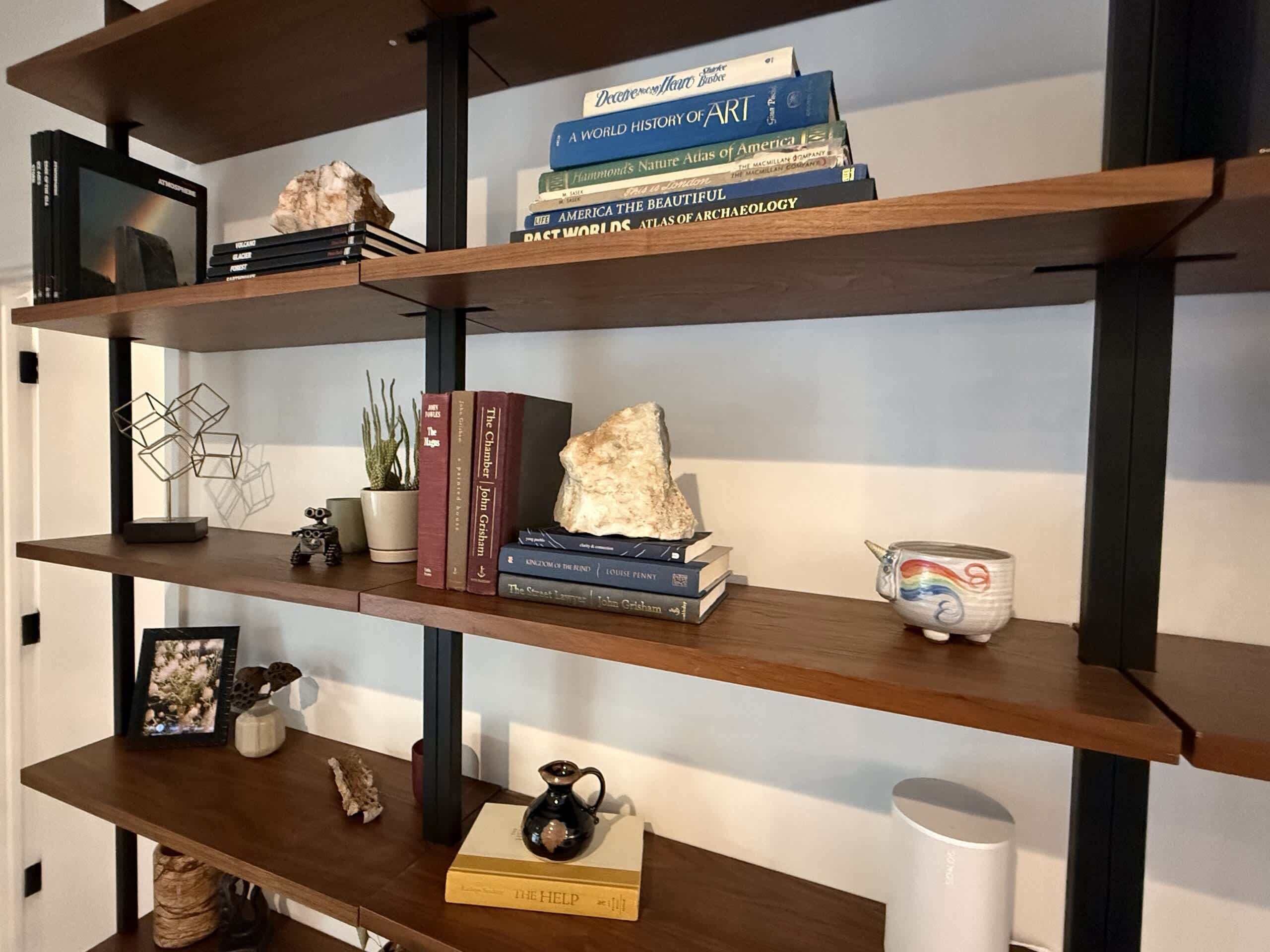 Une bibliothèque avec des livres, un petit cactus, un rocher et un objet décoratif.