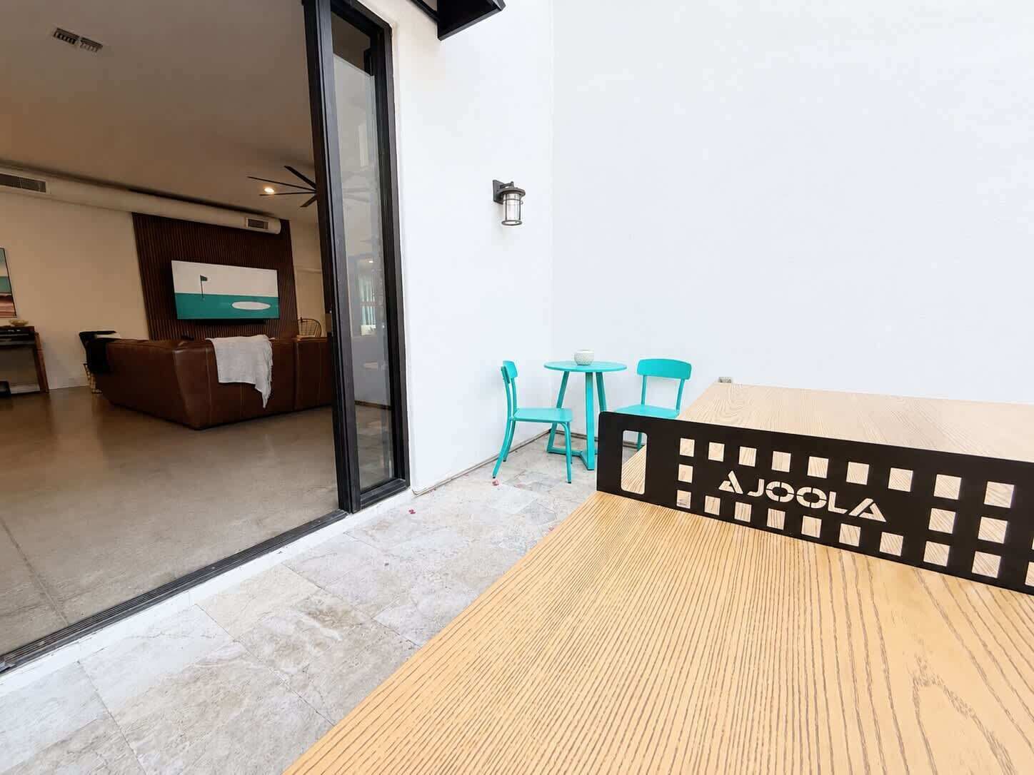 Un intérieur moderne avec une table en bois, des chaises turquoise et une porte vitrée donnant sur un espace de vie.