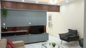 A modern living room with a flat-screen TV, grey sofa, and a grey armchair. - Our house in Praia do Futuro, Fortaleza, offers comfort and privacy, just 100 meters from the sea. (Fortaleza)