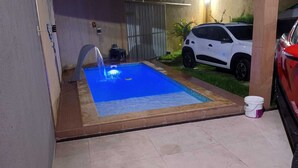 A swimming pool with a water fountain, a white car parked nearby, and a bucket on the ground. - Our house in Praia do Futuro, Fortaleza, offers comfort and privacy, just 100 meters from the sea. (Fortaleza)