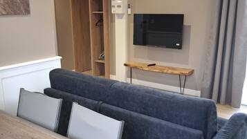Een moderne woonkamer met een hoekbank, een flatscreen televisie aan de muur en een houten salontafel.