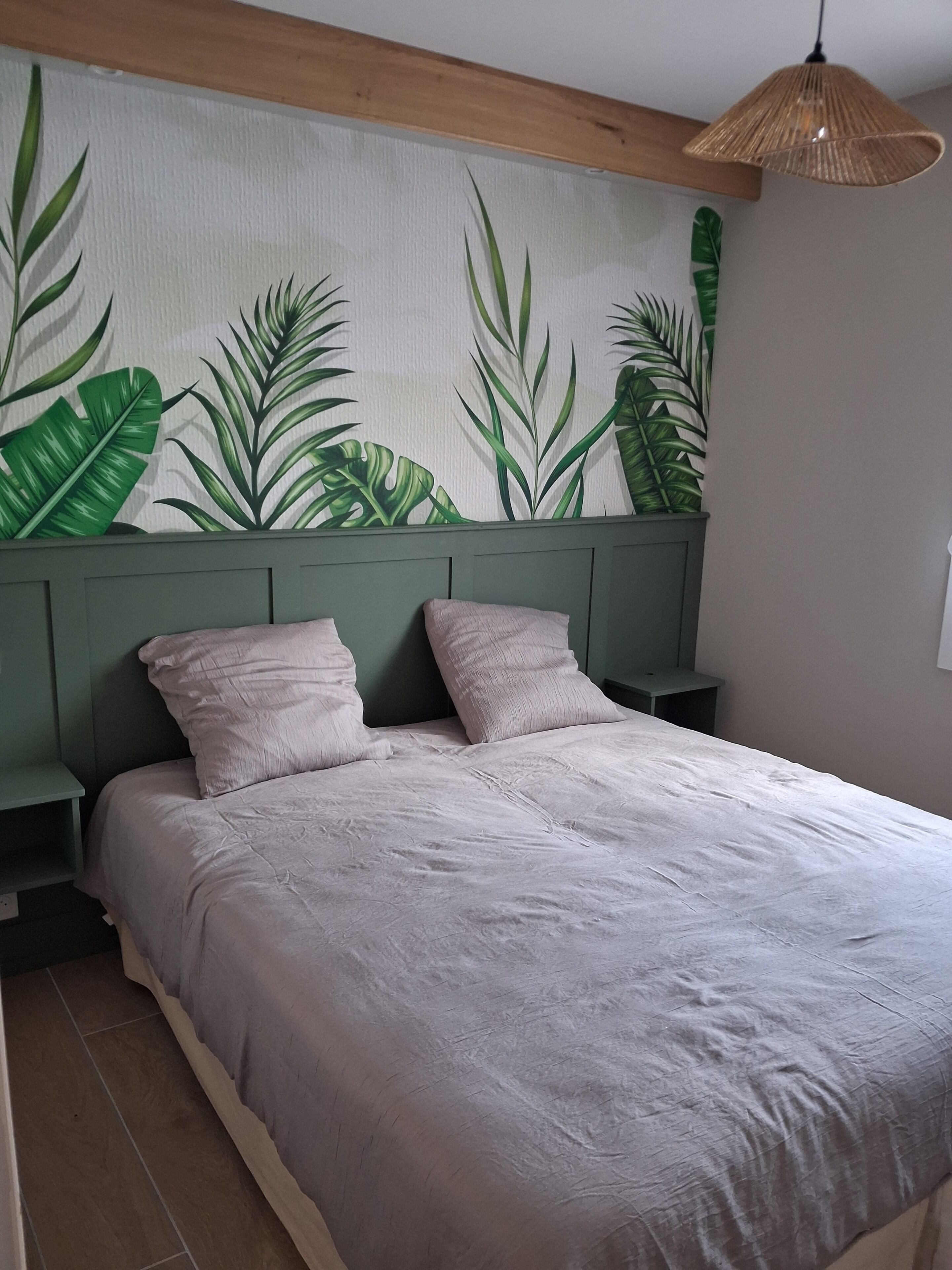 Een slaapkamer met een bed, twee nachtkastjes, een groen hoofdeinde en een muur met een bladmotief.
