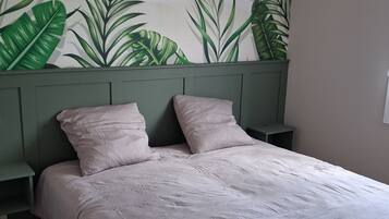 Een slaapkamer met een bed, twee nachtkastjes, een groen hoofdeinde en een muur met een bladmotief.
