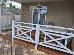 A covered deck with a white railing, a table, and chairs.