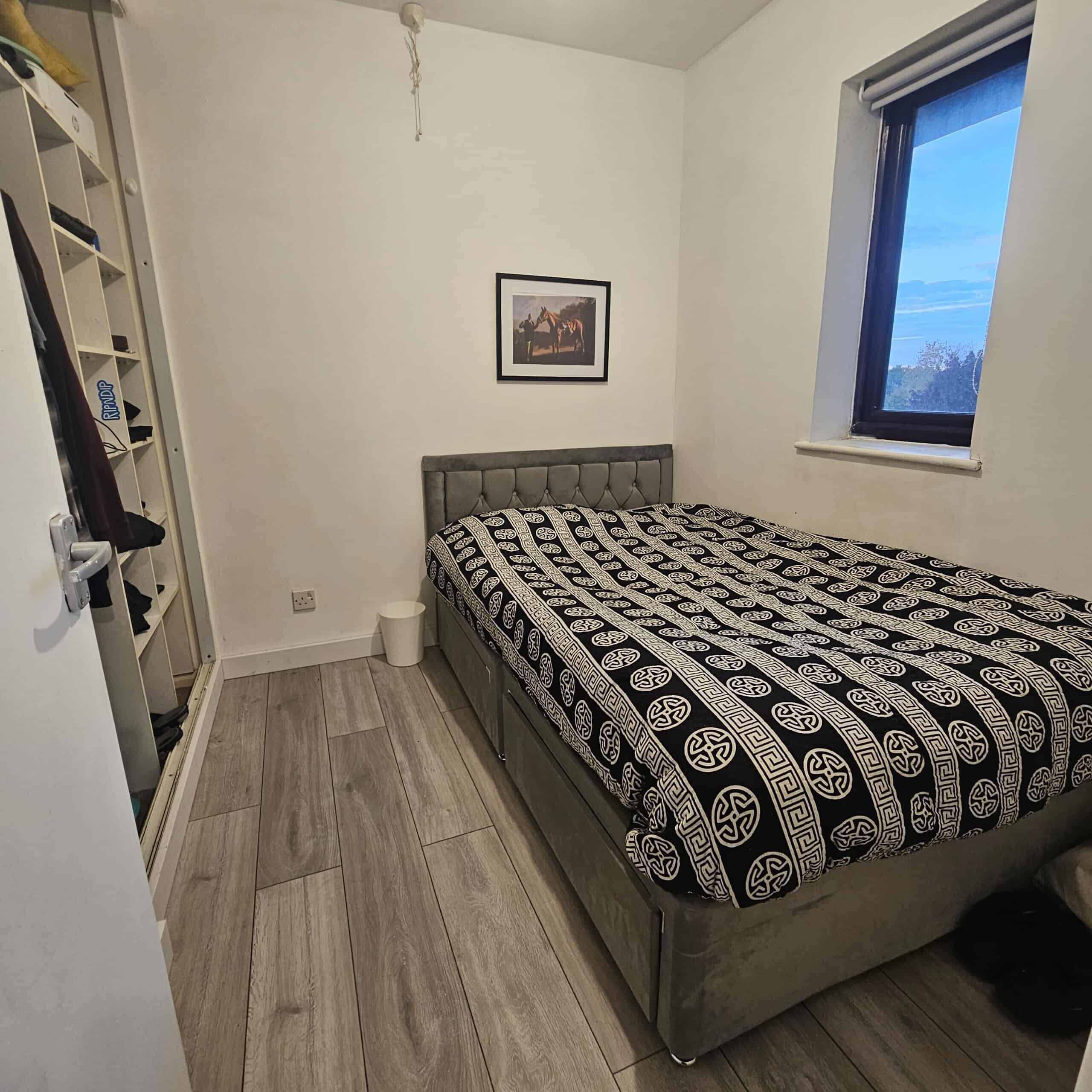 Um quarto com uma cama, uma janela, uma porta e uma pequena imagem na parede.