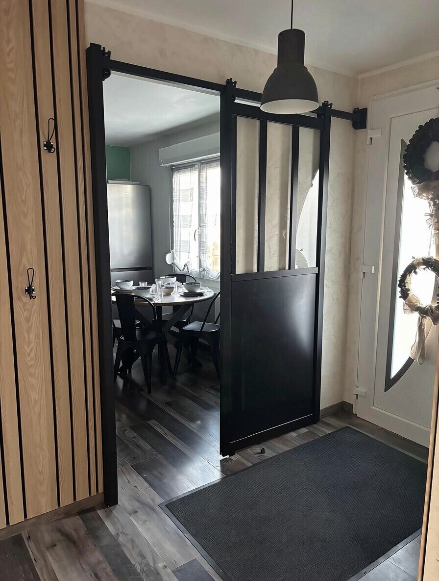 Une pièce dotée d’une porte coulissante donnant sur un coin repas, d’un luminaire suspendu noir et d’un paillasson.