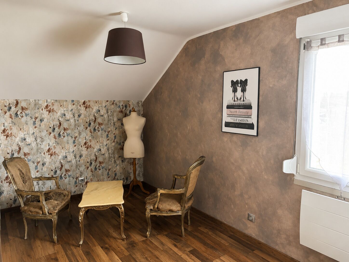Een kamer met een houten vloer, twee antieke stoelen, een tafel, een etalagepop, een wandlamp en een ingelijst schilderij.