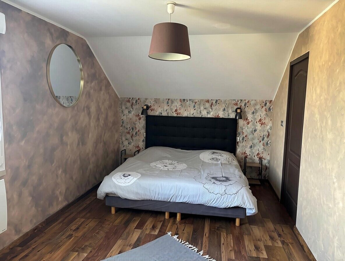 Un dormitorio con cama, un espejo redondo, una lámpara colgante y un papel tapiz estampado.