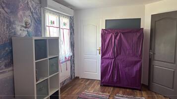 A room with a white bookshelf, a purple wardrobe, a door, and a colorful rug.