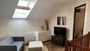 A loft-style room with a sloped ceiling, a sofa, a television, a cabinet, and a staircase. - Le Clos de Candimalo (Epinal–Gérardmer route) (La Baffe)