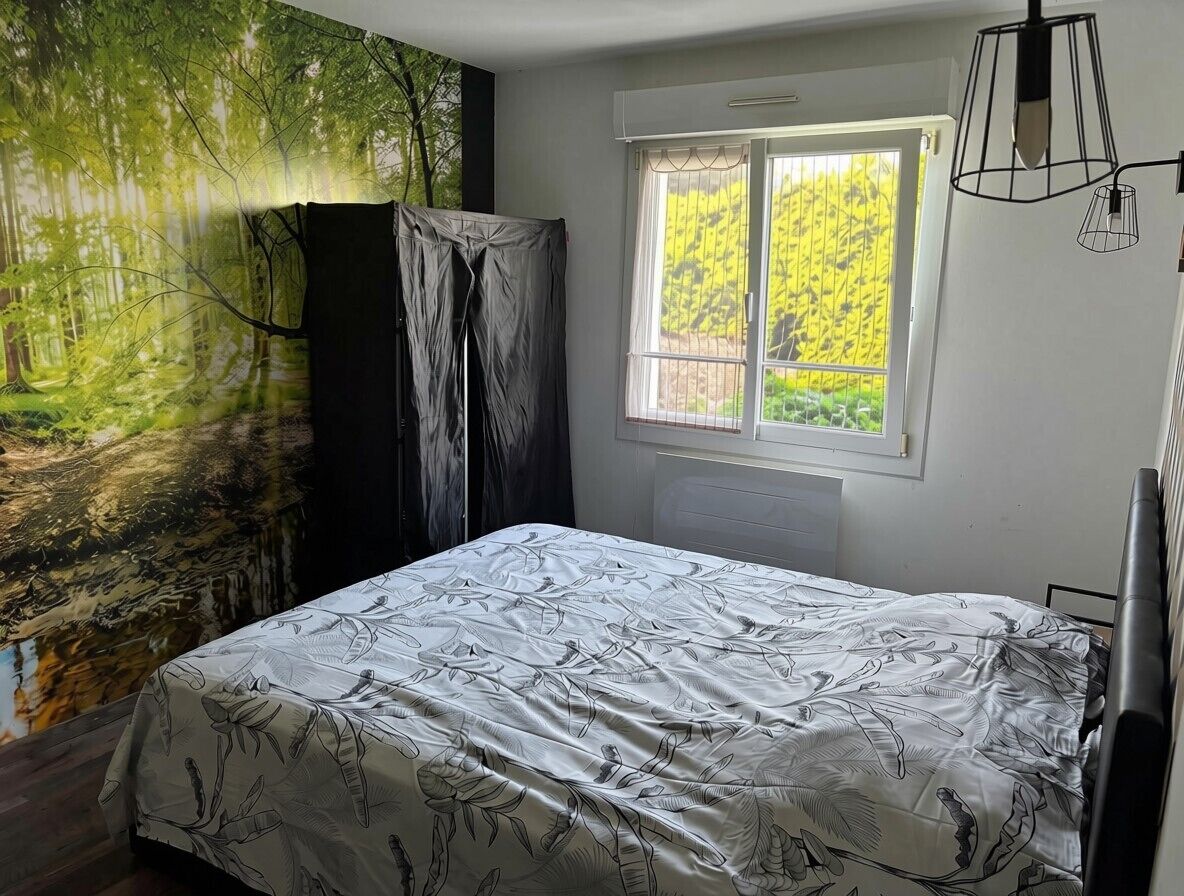 Un dormitorio con cama, una ventana con cortinas, un radiador y un mural en la pared.