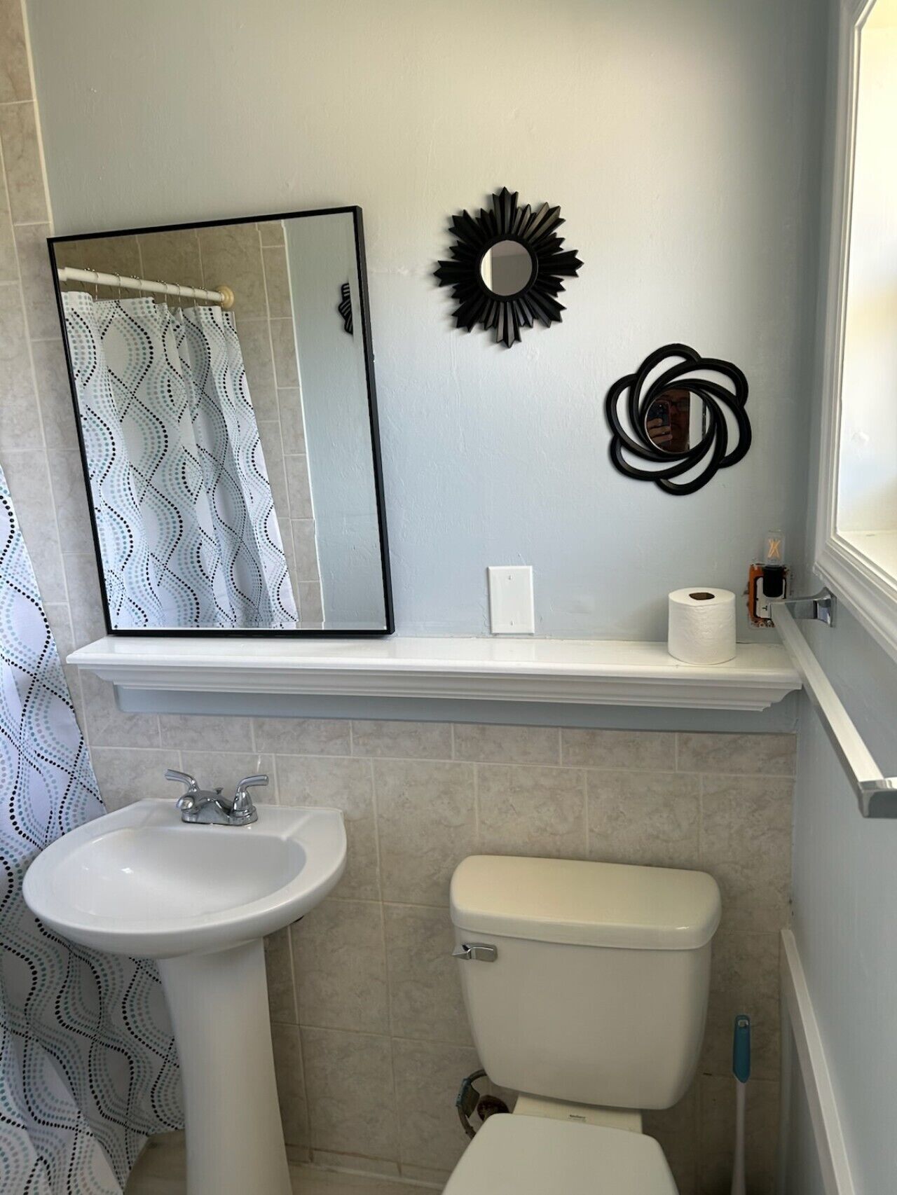 Et badeværelse med vask, toilet, spejl og dekorativ vægkunst.