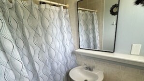 Baño con cortina de ducha, lavamanos, espejo e inodoro.