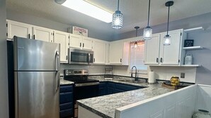A modern kitchen with white cabinets, stainless steel appliances, a granite countertop, and pendant lighting. - Close To The Action Outdoor Pool/ Close Main Strip (Pigeon Forge)