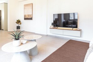 Ein modernes Wohnzimmer mit einem Flachbildfernseher, einem runden Couchtisch, einer Zimmerpflanze und einem großen Teppich.