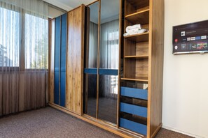 A room with a large wardrobe, a television mounted on the wall, and a window with sheer curtains.