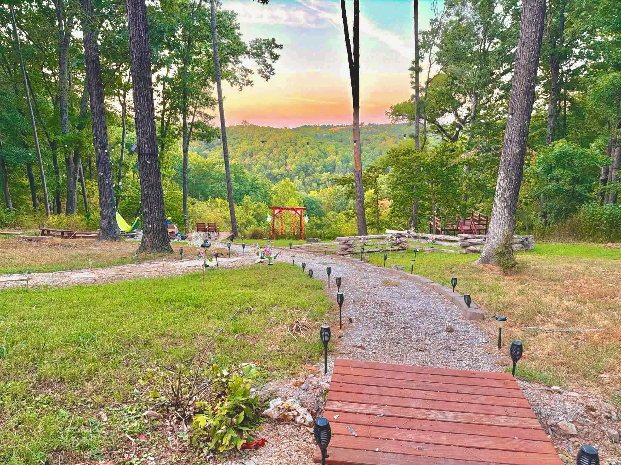A wooden pathway leading through a forested area with a gazebo and picnic tables.