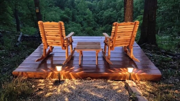 A wooden deck with two rocking chairs and a table, surrounded by a forest. - Mountain Views ,Sunsets, Jacuzzi spa , Kayak to waterfalls,5 mins to Beaver lake (Eureka Springs)