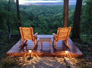 A wooden deck with two rocking chairs and a table, surrounded by a forest. - Mountain Views ,Sunsets, Jacuzzi spa , Kayak to waterfalls,5 mins to Beaver lake (Eureka Springs)