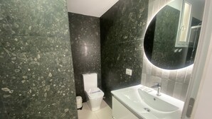 A bathroom with dark speckled walls, a white toilet, a white sink with a mirror, and a white cabinet. - Cozy apartment with fantastic views of Las Vistas Beach (Arona)