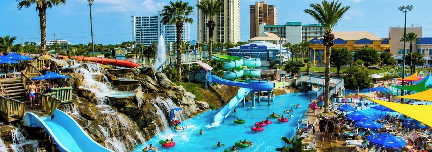 A water park with multiple slides and water features, surrounded by palm trees and buildings.