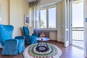Een woonkamer met een blauwe bank, een ronde salontafel en uitzicht op het buitengebied door een raam.