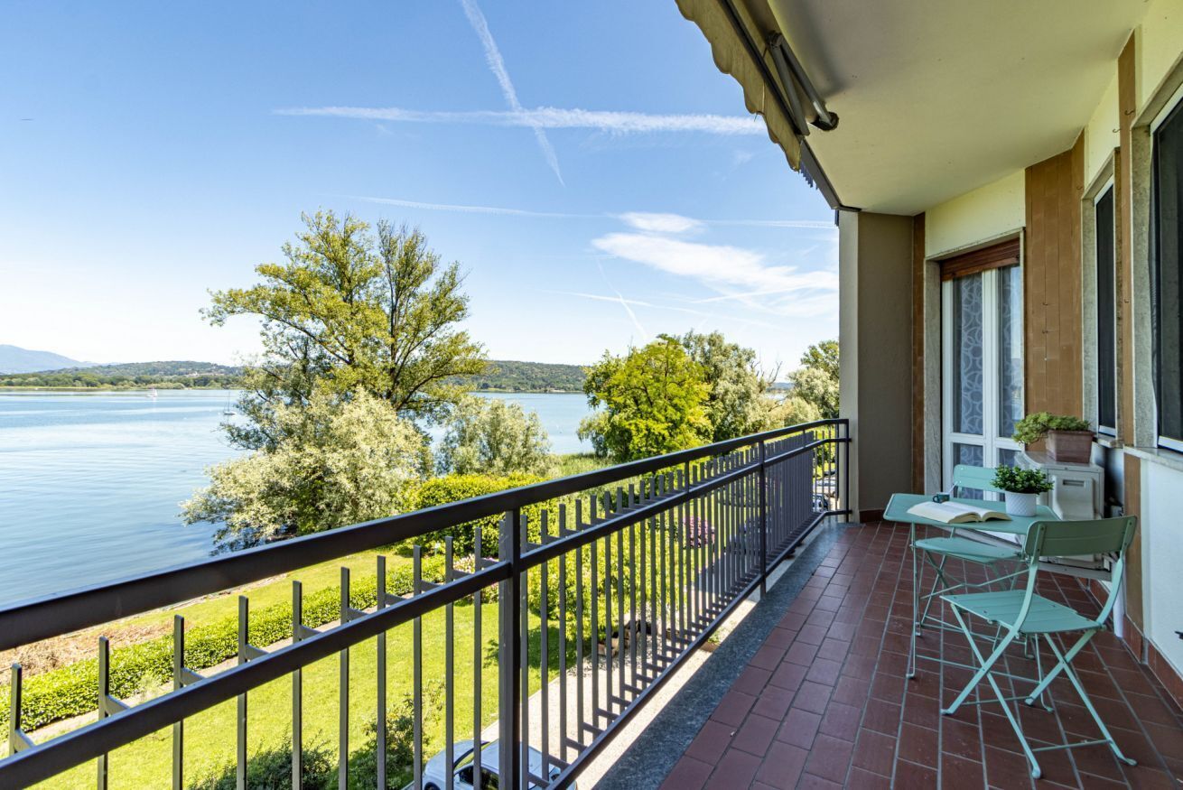 Een balkon met uitzicht op een meer, een hekwerk en een tafel met stoelen.