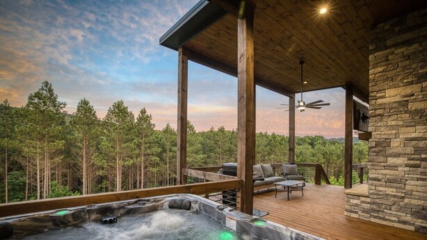 A hot tub on a wooden deck with a stone wall and a view of a forest.