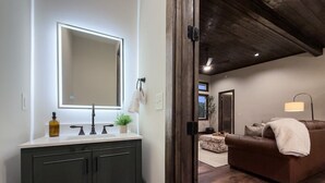 A modern bathroom with a large mirror, dark cabinetry, and a white countertop.