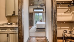 A narrow hallway leading to a bedroom with a bed, a ceiling fan, and a view of the outdoors.