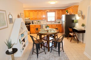 A kitchen with wooden cabinets, a dining table with chairs, a refrigerator, and a small side table with a plant. - Whispering Cove | Elegant Water View Retreat at Wilson Lake (Muscle Shoals)