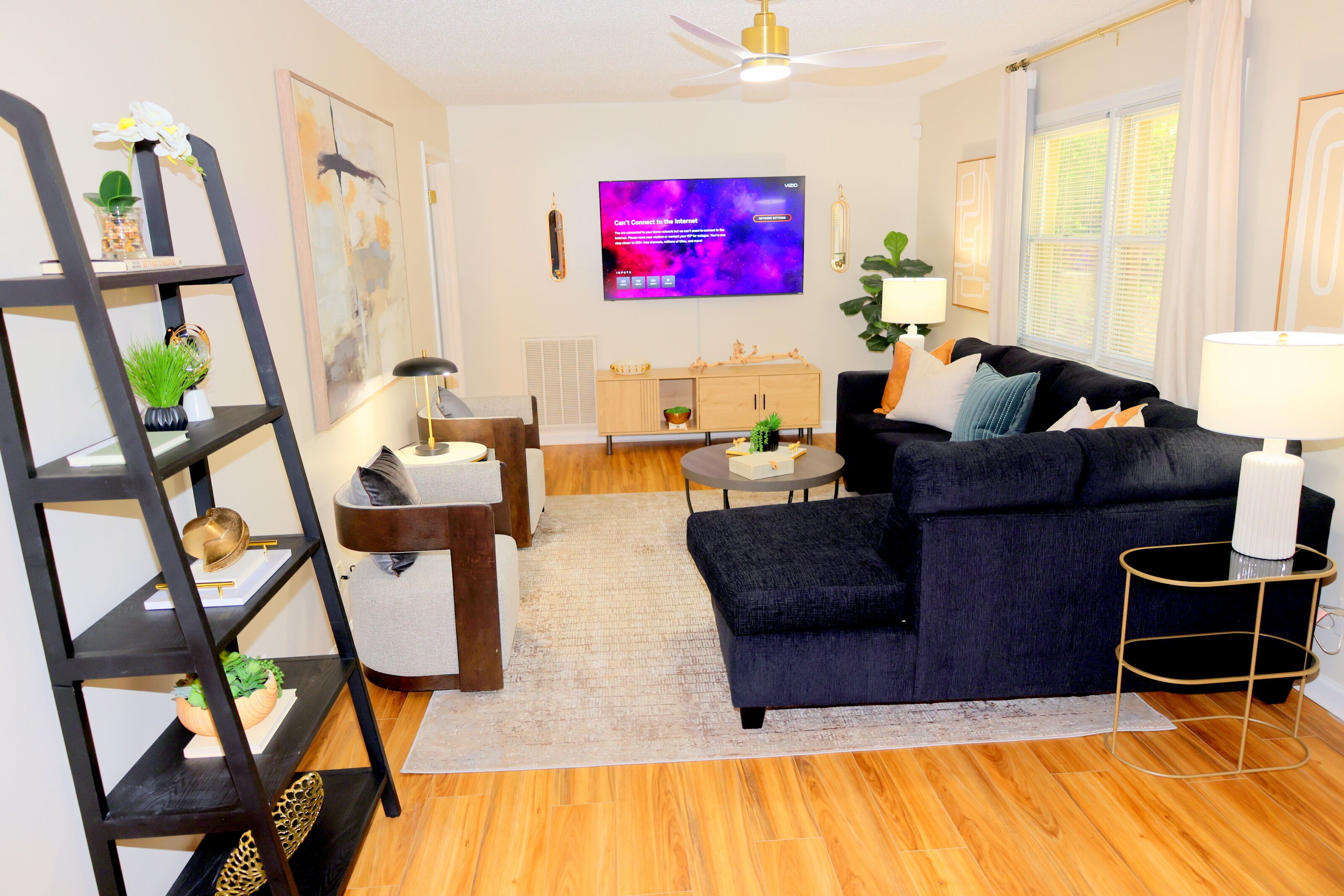 A living room with a dark blue sofa, a wooden coffee table, a black bookshelf, a TV on the wall, and a ceiling fan.