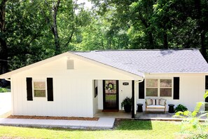 A single-story house with a front porch, a number '175' sign, and a bench with potted plants. - Whispering Cove | Elegant Water View Retreat at Wilson Lake (Muscle Shoals)